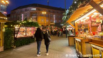 People walk down a nearly empty path next to stalls at the Christmas market.
