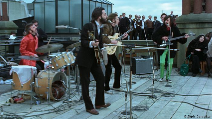 A still from 'Get Back': Ringo Starr, Paul McCartney, John Lennon, and George Harrison performing for a gathered crowd on a rooftop.