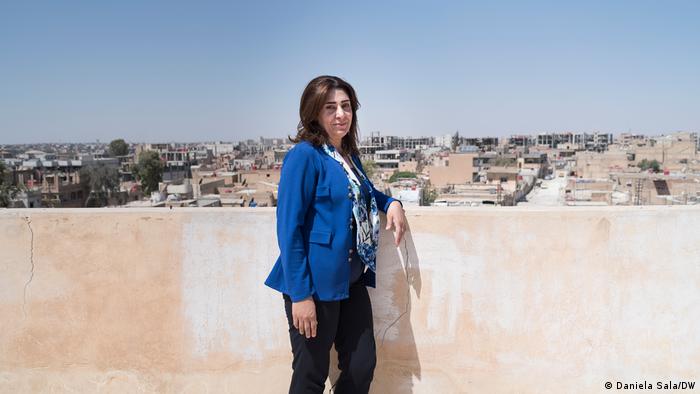 Eine Frau lehnt an einer Mauer, im Hintergrund das Stadtbild von al-Hasaka, Nordsyrien
