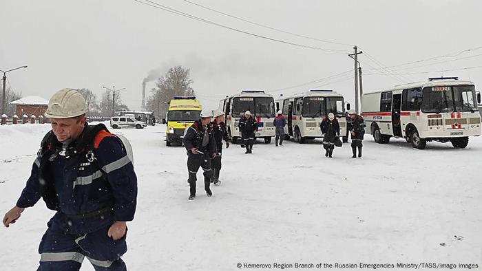 Men in safety helmets in the snow with emergency vehicles in background