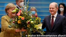 German Chancellor Angela Merkel, left, receives a bouquet from Vice Chancellor and Finance Minister Olaf, Scholz, right, prior to the cabinet meeting at the chancellery in Berlin, Germany, Wednesday, Nov. 24, 2021. Merkel was given flowers as this was probably her last cabinet session as German Chancellor as negotiations are going on to form a new government after elections were held in September. (AP Photo/Markus Schreiber, Pool)