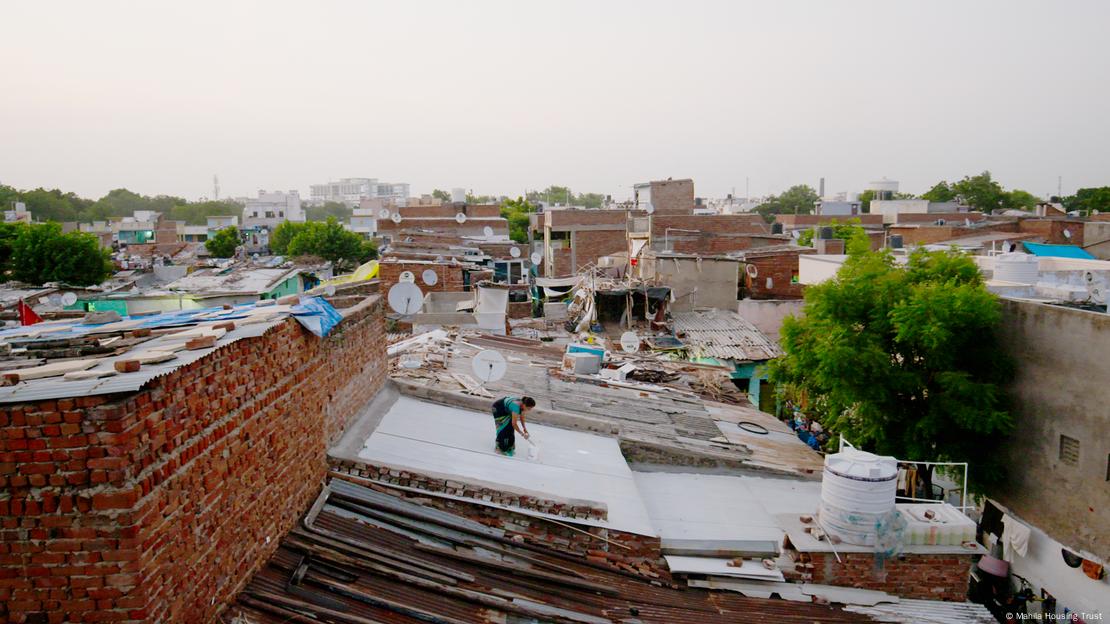 A woman paints her rooftop with solar reflective white paint in Ahmedabad, India