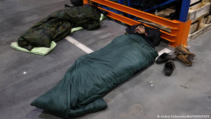 Des migrants se reposent dans des sacs de couchage sur un sol en béton