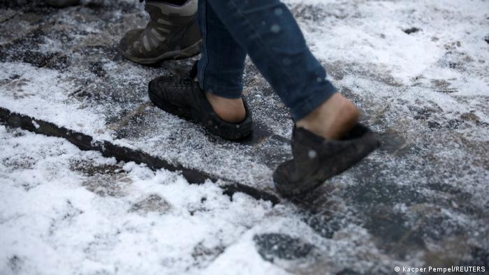A closeup of a person walking on a snowy path, wearing sandals and no socks