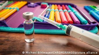 Ампула и шприц с вакциной на фоне школьного пенала с фломастерами