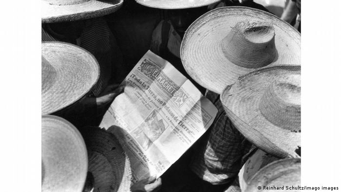 A photo of people from above shows the top of large straw hats and a newspaper.