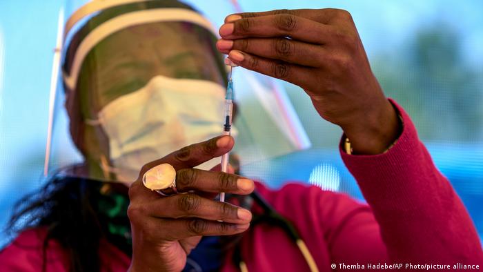 A health worker wearing a mask and a visor draws up a dose of a BioNTech-Pfizer vaccine into a needle