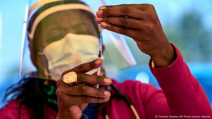 A health worker wearing a mask and a visor draws up a dose of a Pfizer vaccine into a needle