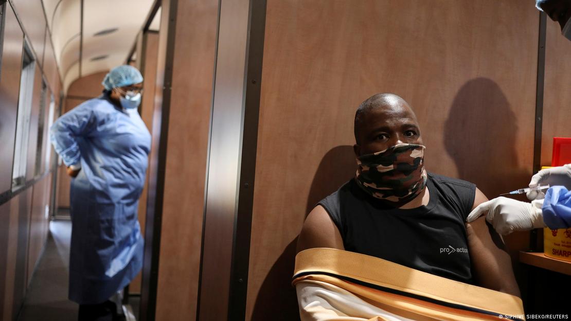 Homem negro e com máscara de pano recebe vacina. 