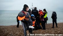 TOPSHOT - A migrant carries her children after being helped ashore from a RNLI (Royal National Lifeboat Institution) lifeboat at a beach in Dungeness, on the south-east coast of England, on November 24, 2021, after being rescued while crossing the English Channel. - The past three years have seen a significant rise in attempted Channel crossings by migrants, despite warnings of the dangers in the busy shipping lane between northern France and southern England, which is subject to strong currents and low temperatures. (Photo by Ben STANSALL / AFP) (Photo by BEN STANSALL/AFP via Getty Images)