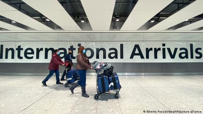 People pushing suitcases walk in front of an international arrivals sign in Heathrow