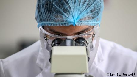 A medical technology student wearing protective gear looks through a microscope in Manila