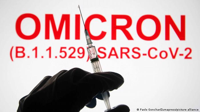 A hand holding a medical syringe with a text Omicron (B.1.1.529): SARS-CoV-2 in the background