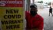 Homem ao lado de cartaz com as palavras, em inglês: Nova variante da covid aqui Homem ao lado de cartaz com as palavras, em inglês: Nova variante da covid aqui