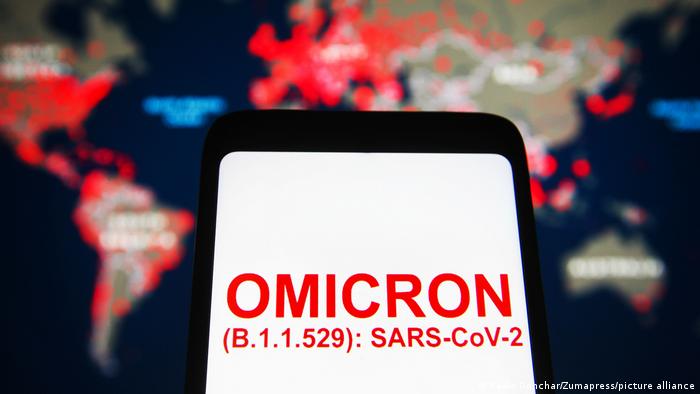 The word omicron on smartphone display in front of a world map showing the spread