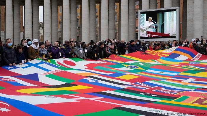 Members of a migrants association hold a huge banner made with world's flags as Pope Francis deliver the Angelus prayer in St. Peter's Square at the Vatican, on Sunday