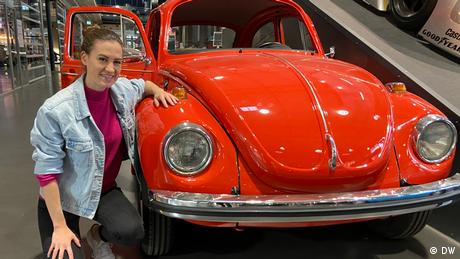 Rachel Stewart von Meet the Germans kniet neben einem roten VW-Käfer