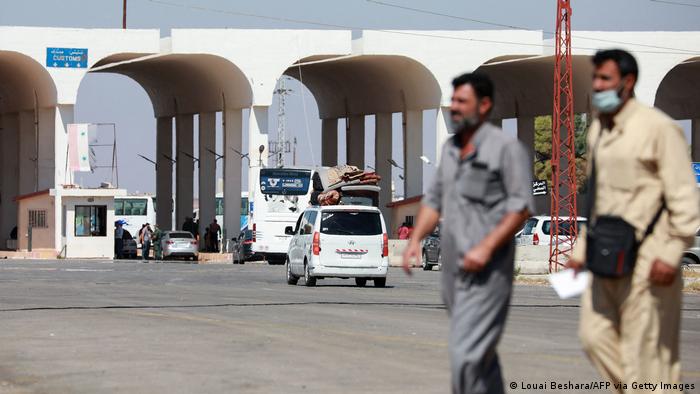 Two men walk past cars and busses at the Syria-Jordan border