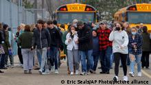 Parents walk away with their kids from the Meijer's parking lot, where many students gathered following an active shooter situation at Oxford High School, Tuesday, Nov. 30, 2021, in Oxford, Mich. Police took a suspected shooter into custody and there were multiple victims, the Oakland County Sheriff's office said. (Eric Seals/Detroit Free Press via AP)