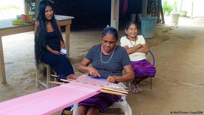 Indigene Weberinnen in Mexiko: Drei Frauen sitzen auf Stühlen, eine von ihnen webt ein großes Stück Stoff