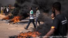 Pedestrians walk next to fires during a demonstration in Ouagadougou on November 27, 2021. - Anti-riot police fired tear gas to prevent the demonstrators from gathering in a square in the centre of Ouagadougou, where substantial police and security forces were deployed and all shops closed. (Photo by OLYMPIA DE MAISMONT / AFP)