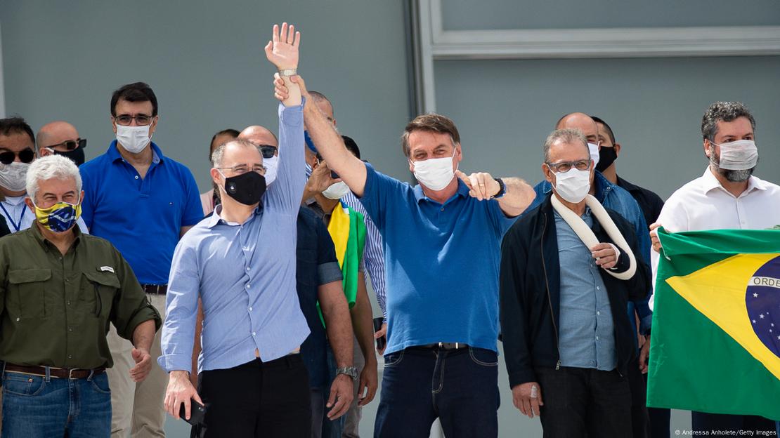 Em foto externa, Bolsonaro ergue o braço de Mendonça em evento com outros políticos ao lado.