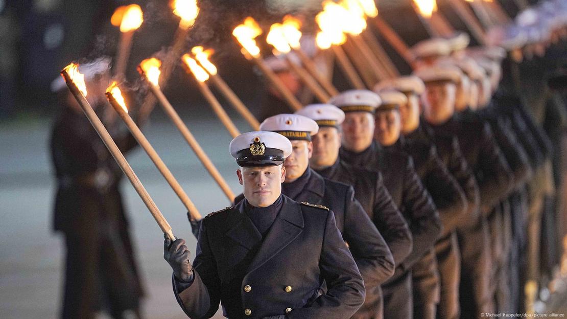 Fila de militares erguendo tochas durante cerimônia de despedida de Angela Merkel