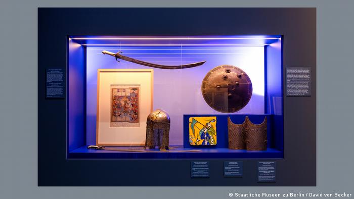 A museum display with an ancient sword, shield, helmet and different paintings. 