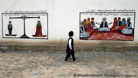 یک کودک افغان در جاده ای در کابل، از کنار نقاشی های دیواری عبور می کند. نقاشی دیواری سمت چپ از این ایده حمایت می کند که شهروندان زن و مرد طبق قوانین افغانستان از حقوق برابر برخوردارند. دیگری به مسائل ازدواج می پردازد و مدعی است که در اسلام ازدواج اجباری وجود ندارد. دو حق بشری که پس از آمدن طالبان همواره نقض گردیده اند.