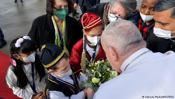 Paus membungkuk untuk mengambil buket bunga dari sekelompok anak-anak dengan pakaian tradisional