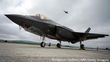 A Lockheed Martin F-35 Lightning II fighter jet is parked on the tarmac at the Payerne Air Base as a Boeing McDonnell Douglas F/A-18 Hornet takes off in the background, during flight and ground tests, as Switzerland is looking for a new fighter jet to replace its aging fleet, on June 7, 2019 in Payerne. (Photo by Fabrice COFFRINI / AFP) (Photo credit should read FABRICE COFFRINI/AFP via Getty Images)