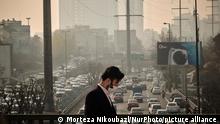 An Iranian man wearing a protective face mask walks along a street-side in northern Tehran during a polluted air, following the COVID-19 outbreak in Iran, on January 12, 2021. Tehran is wedged between mountains and dirty air can get trapped when there is no wind or rain. Iranian health experts say thousands of deaths a year are caused by heart attacks and respiratory illnesses brought on by smog. (Photo by Morteza Nikoubazl/NurPhoto)