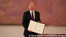 A smiling Olaf Scholz holding his certificate of appointment to the cameras