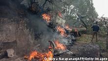 A man stands next to the burning debris of an IAF Mi-17V5 helicopter crash site in Coonoor, Tamil Nadu, on December 8, 2021. - A helicopter carrying India's defence chief General Bipin Rawat crashed, the air force said, with a government minister at the scene saying at least seven people were dead. (Photo by Surya NARAYANAN / AFP) (Photo by SURYA NARAYANAN/AFP via Getty Images)