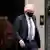 Boris Johnson de máscara, terno e gravata deixa Downing Street. Há uma coroa de Natal na porta. 
