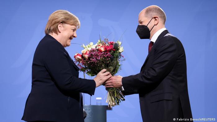 Olaf Scholz hands Angela Merkel flowers