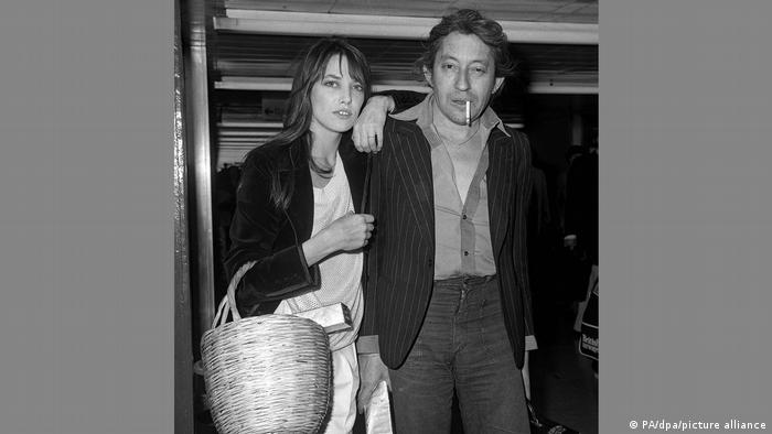 60s and 70s style icon Jane Birkin has a wicker basket hanging from one arm while she rests her other arm on the shoulder of her then-partner, French musician Sege Gainsbourg
