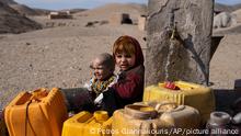 Two Afghan children sit next to a spigot as people of Kamar Kalagh village outside Herat, Afghanistan, try to fill their plastic containers with water, on Friday, Nov. 26, 2021. Afghanistan’s drought, its worst in decades, is now entering its second year, exacerbated by climate change. (AP Photo/Petros Giannakouris)