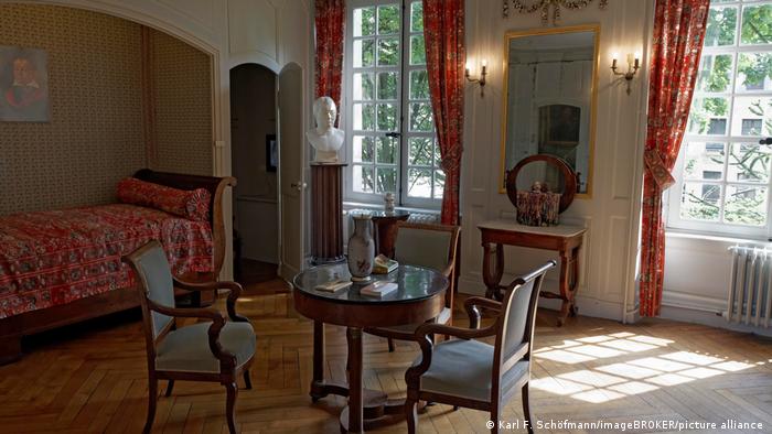 Ein altes Wohnzimmer mit Büste und drei Stühlen um einen kleinen runden Tisch und blauen Polstern