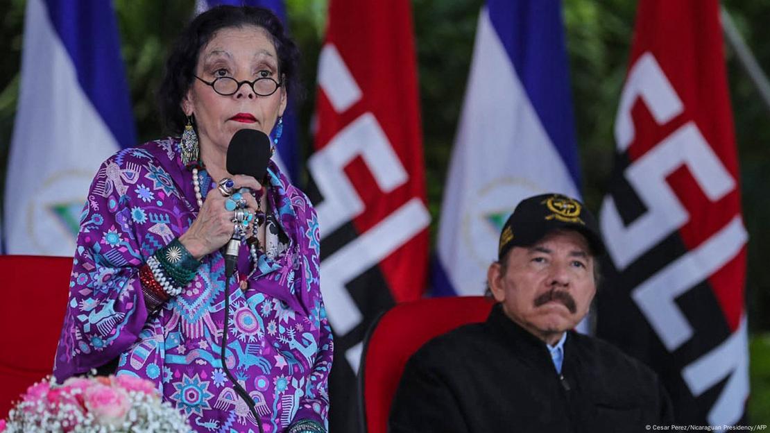 Vice-presidente Rosario Murillo, de pé com microfone na mão, é esposa do mandatário da Nicarágua, Daniel Ortega, sentado, de bigode e boné na cabeça