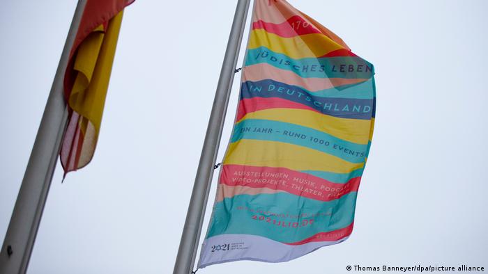 Eine bunte Flagge mit der Aufschrift Auf das Leben! und dem Hinweis auf das Festjahr „1700 Jahre jüdisches Leben in Deutschland“ an einer Fahenstange. 