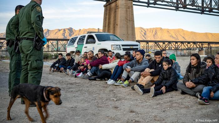 Migrants sit in a line, facing US border guards in New Mexico