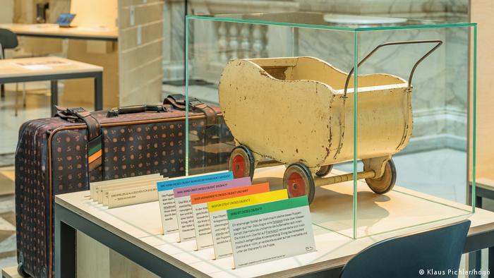 The doll's carriage in the vitrine and the suitcase next to it.