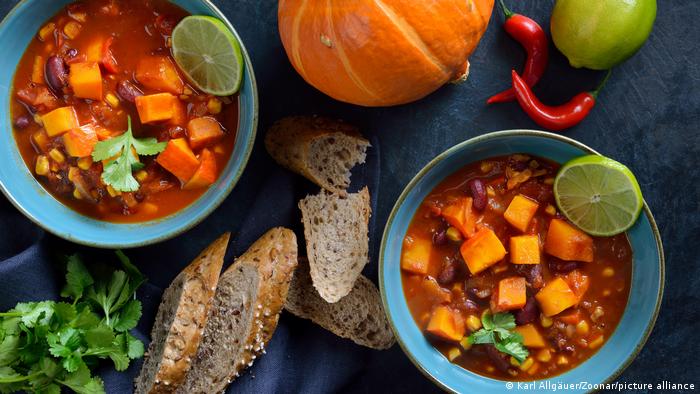 Hot vegan chili con calabaza from the vegan cuisine with lime and coriander served with slices of a wholemeal roll.