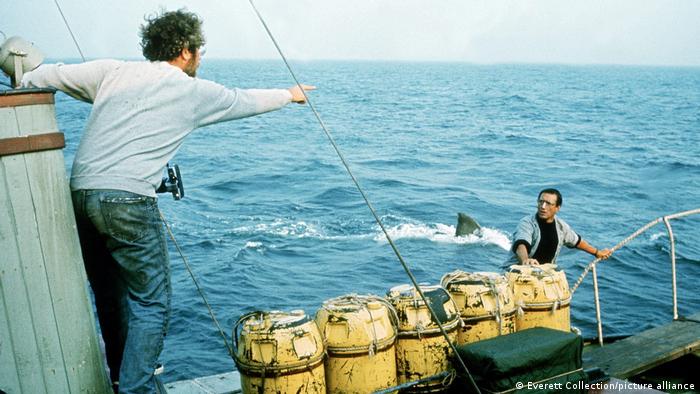 A still from the film Jaws with one man on a boat pointing to an approaching shark as another is gets onto the boat