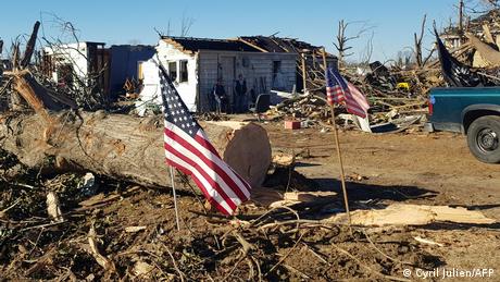 People stand in front of their destroyed home in Mayfield, Kentucky, with two American flags in the foreground