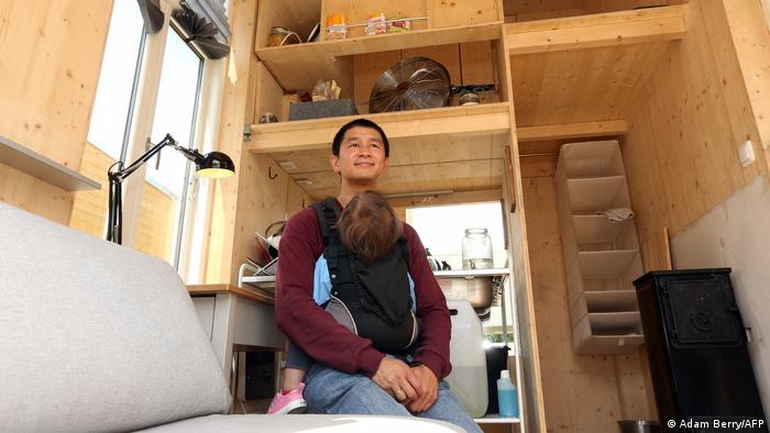 Van Bo Le-Mentzel sits in a tiny house in Berlin with his child in a sling around his chest