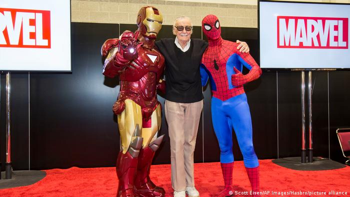 Stan Lee posiert mit seinen Figuren Iron Man und Spider-Man auf dem roten Teppich. 