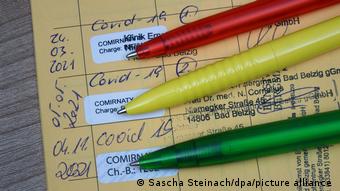 Паспорт вакцинации с тремя вклейками о прививке против ковида и лежащими напротив них шариковыми ручками разных цветов: красной, желтой и зеленой