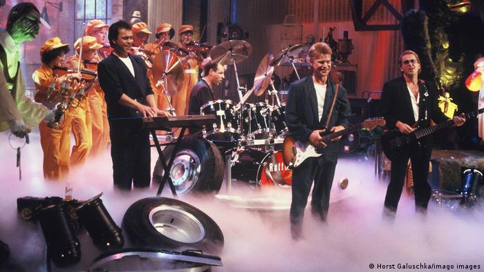 Band performing amid tires and fog on a TV set.